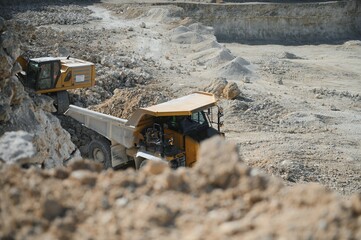 Large quarry dump truck. Big yellow mining truck at work site. Loading stone into body truck