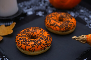 two donuts with orange glaze and sprinkles on a board in close-up