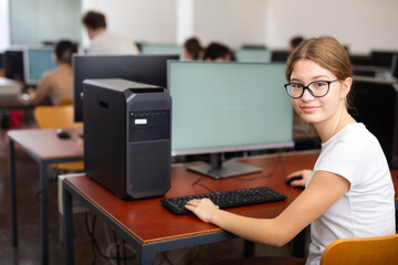 Young girl student turned around and looking at camera during lesson in college computer class