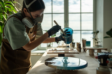 Serious female artist works with epoxy resin, creating picture in technique of liquid art....