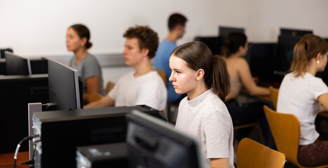 Fototapeta premium Teenage girl sitting at table and using computer during lesson.