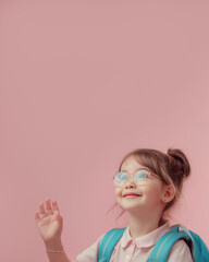 Fototapeta premium Smiling schoolgirl with backpack waving and looking up on pink background