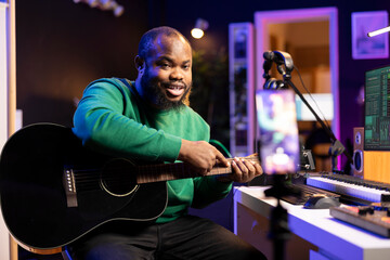 Guitarist instructor hosting guitar lessons online using a mobile phone, recording video tutorial for master class. Artist musician explaining acoustic instrument accords, assistance for beginners.