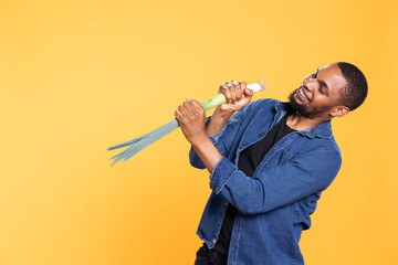 African american charismatic guy pretend singing on a leek, mimicking a performance on microphone...