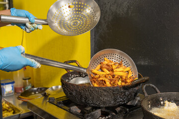 Cook removing french fries from deep fryer with metal strainer