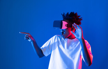 Young African American gaming player wearing VR pointing hologram 3D graphic isolated blue pink...