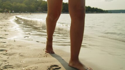 A close-up shot of a girl little feet walking along the beach at sunset. The soft sand cradles her steps, leaving a trail of footprints as the golden rays of the sun illuminate the coastal strip. - Powered by Adobe
