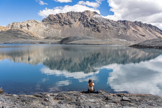Woman sitting on a rock looking at a mountain in the morning light with an amaizing lagoon infront of her with blue and clouds whit colors