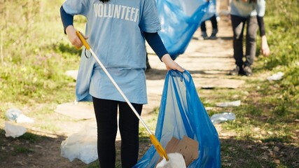 Young child using tongs tool to grab and pick up trash from the woods, collecting rubbish from a...