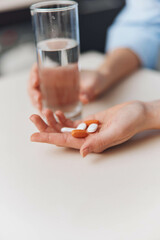 Woman holding pills and glass of water on table in front of her, healthcare and medication concept