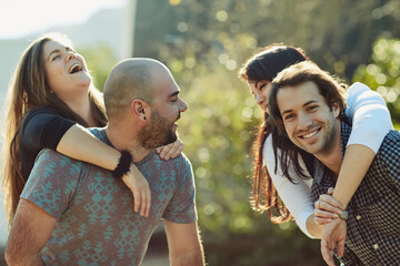 Fototapeta premium Happy, people and couple with piggyback outdoor for summer vacation, reunion date and playful bonding. Smile, friends or fun with embrace for holiday care, loyalty support and game together of travel