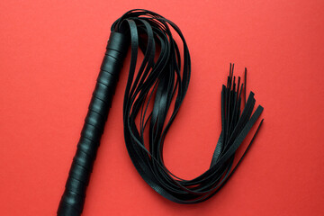 Leather black whip for sex games on a red background. BDSM toys for role-playing sex games.