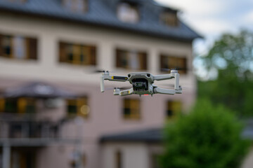 A small drone hovering with a building in the background.