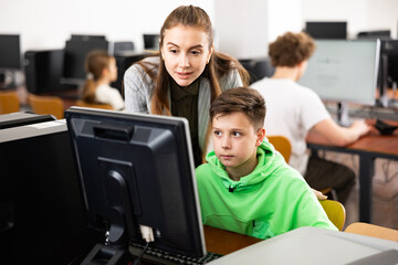 Fototapeta premium Teacher explaining task solution to teenage boy during computer science lesson in school.