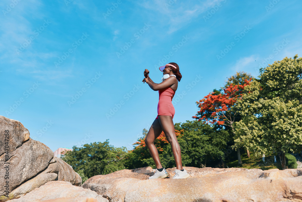 Wall mural woman in sporty outfit exercising on rocky terrain under a clear blue sky