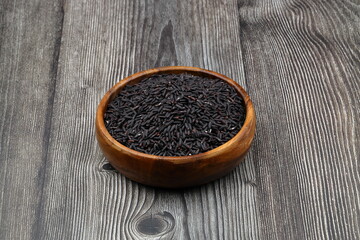 pile of black rice in a wooden bowl on a wooden table close-up