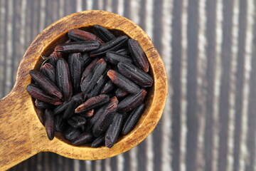 Black wild rice with bamboo spoon on wooden background