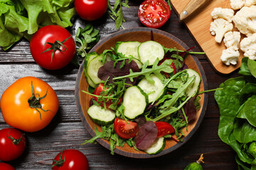 Healthy vegetarian food. Salad in bowl and vegetables on wooden table, flat lay
