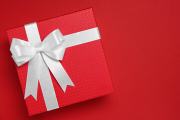 Gift box with white bow on red background, top view. Space for text