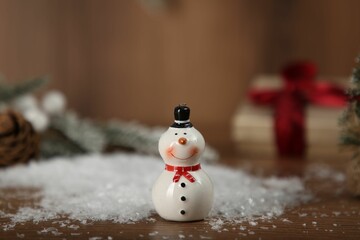 Cute decorative snowman with artificial snow on wooden table, closeup