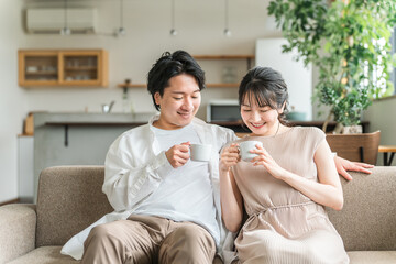 家のリビング・ソファでくつろぐ仲良しの若い日本人夫婦
