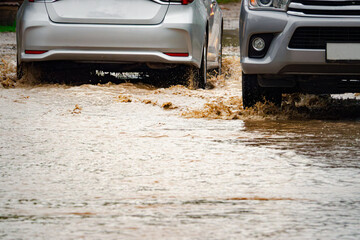 Two cars are driving through a flooded street. The water is up to the hood of one of the cars