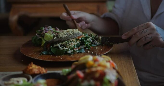 Close-up of cutting creamy vegan calzone filled with lots of vegetables and greens with cutlery. Plant-based lunch options