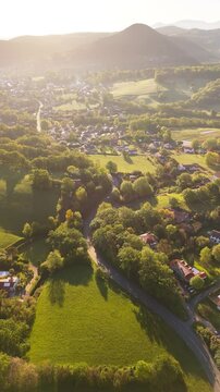 Aerial view of a picturesque village surrounded by lush fields and tranquil mountains at sunset, Ascain, Basque Country.