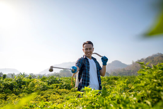 An Indonesian farmer man is standing in a field with a pesticide spray in his hand