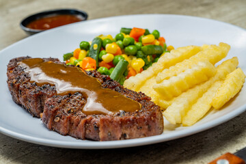 A plate of food with a piece of sirloin meat, vegetable mix, and french fries