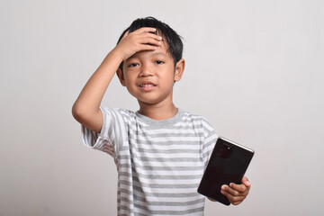 Sad Asian boy looking at smartphone with hand on head isolated on white background. little boy holding phone. he is shocked by what he sees.