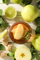 Glass with apple cider, mint branches and apples on light wooden background, top view
