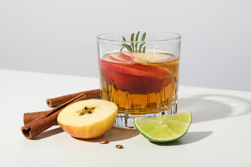 Glass with apple cider, cinnamon sticks, lime and apple pieces on white background, close up