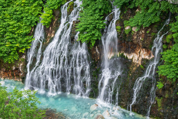 Obraz premium 青い川に流れ落ちる緑に包まれた白ひげの滝