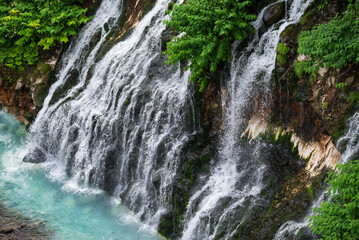 青い川に流れ落ちる緑に包まれた白ひげの滝