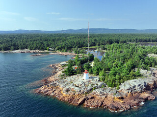 Old lighthouse on a rocky outcrop on Lake Huron's northern shore with forest and mountains in the background