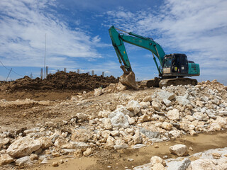A green excavator is in a pile of rocks in the constructions or civil engineering project