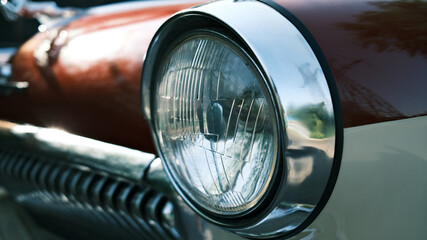 Vintage car headlight close-up. Classic automobile front light detail. Retro vehicle chrome trim...