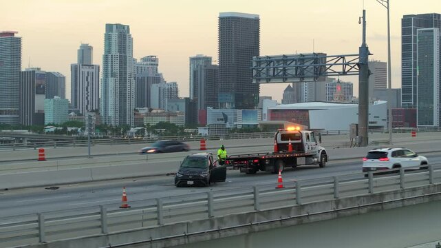 Traffic accident with tow truck hauling smashed vehicle on car crash site. First responders helping on road emergency in Miami Florida, USA