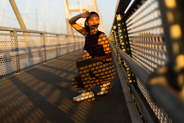 Stylish woman enjoys a sunny afternoon on a bridge, sipping water while basking in the golden glow...