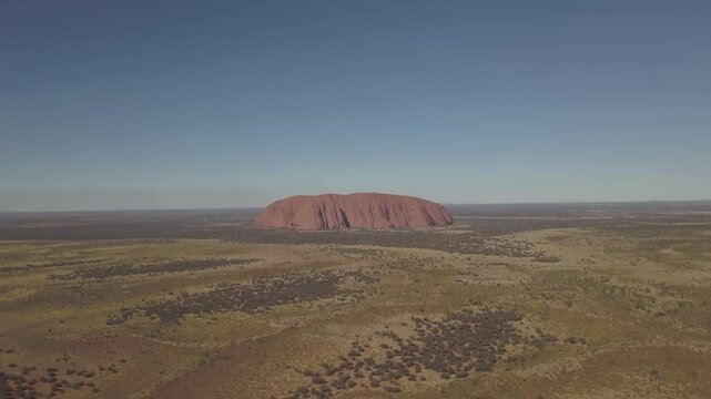 Aerial view of the iconic Uluru rock formation in a vast arid desert under a clear sky, Yulara, Australia.