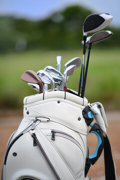 close up of the white golf bag besides the faieway and Inside the bag have various kind of golf clubs.