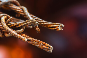 Rusty twisted broken steel wire on red toned background, close-up view, represents war, danger, social issues concept