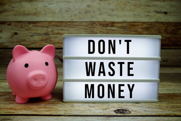 Don't waste money text on LED lightbox with piggy saving on wooden background, Money concept
