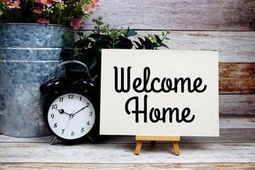 Welcome Home text with alarm clock on wooden background