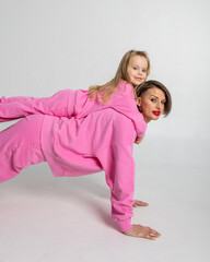 Young mother and little daughter walking holding hands. Dressed in pink color suits on white background, studio. Concept of advertising positive and clothes. Vertical photo