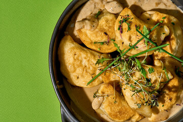 A close-up of a cast iron skillet filled with golden-brown, baked varenyky. The varenyky are garnished with fresh herbs on green background.