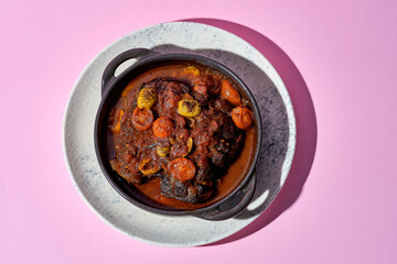 A hearty portion of braised beef cheeks in a rich tomato sauce. The dish is served in a cast iron skillet and garnished with fresh herbs.