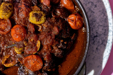 A hearty portion of braised beef cheeks in a rich tomato sauce. The dish is served in a cast iron skillet and garnished with fresh herbs.
