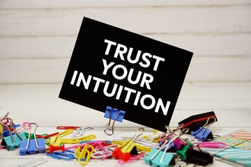 Trust Your Intuition text on paper card with stationary on wooden background